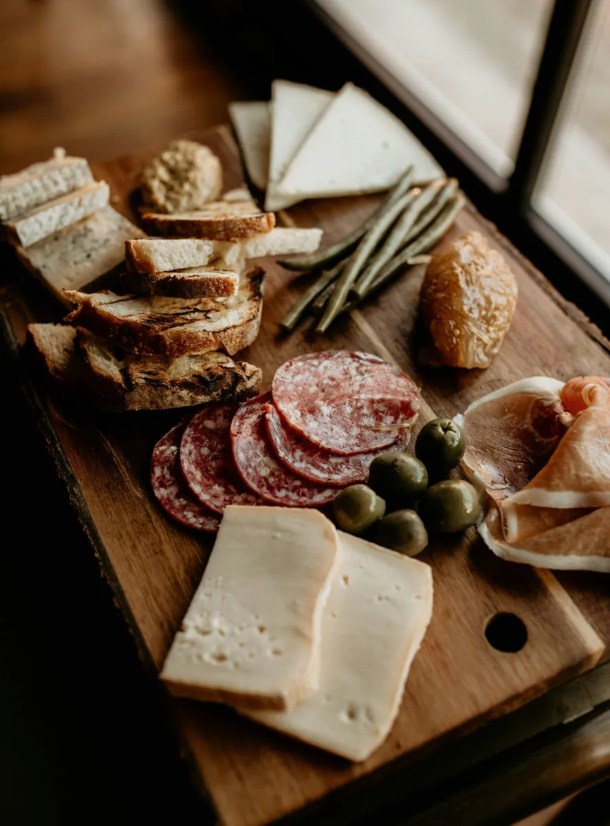 Wooden board with soft cheese, cured meat slices and fresh bread