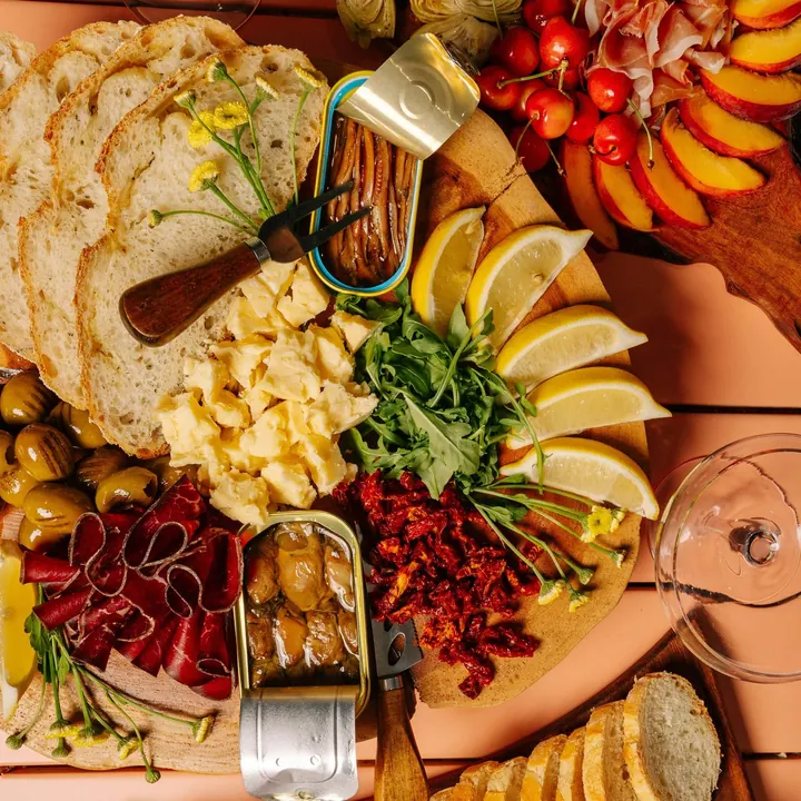 Bread, olives, lemon, cheese and cured meats on a peach-coloured board